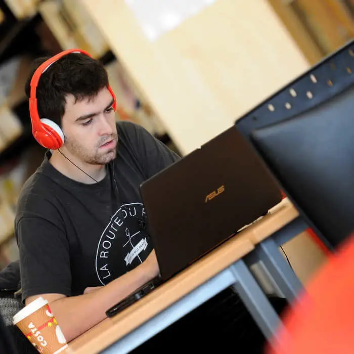 male students with headset working on a laptop in the library of СʪƵ London